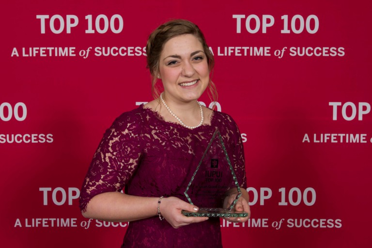 Sarah Grace Fraser stands in front of event backdrop holding Most Outstanding Student award