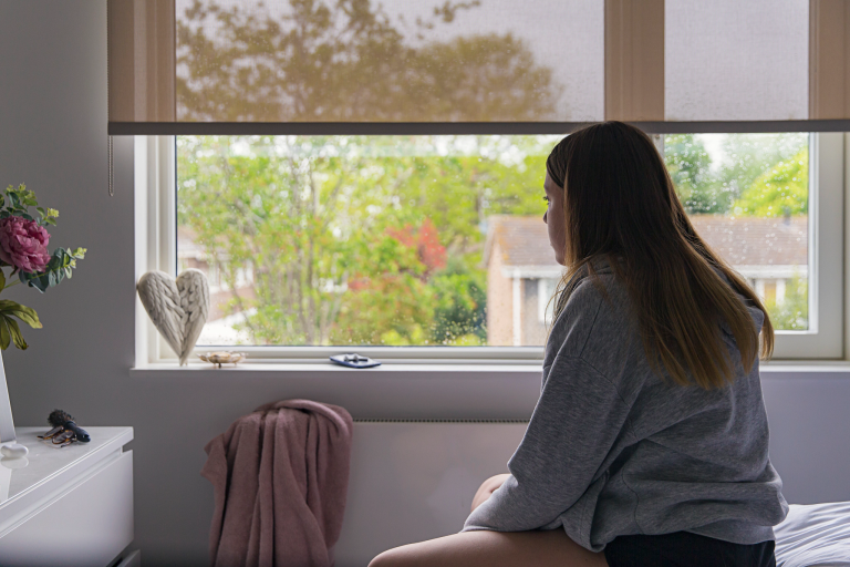 A girl sits on a bed looking out the window