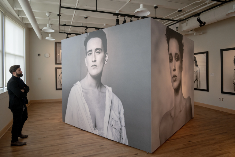 A man in a suit stands and looks at a mural-sized photograph of an androgynous model.
