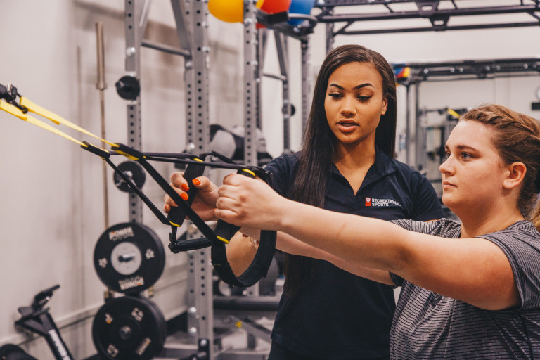 A member of Campus Recreation instructs an exercising student.