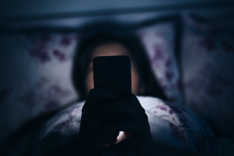 Person looking at cell phone while lying in bed