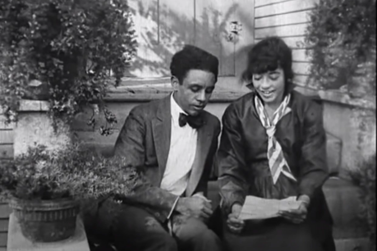 A black-and-white image of a well-dressed Black man and woman sitting on a stoop together.
