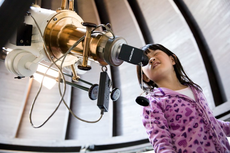 A young girl looks through a telescope