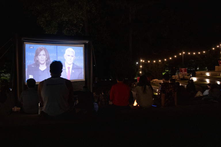 Students watch the vice presidential debate on a large screen outdoors
