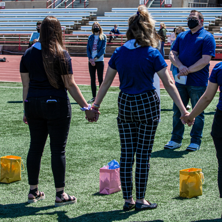 Students standing in Carroll Stadium holding hands and listening to a speaker.
