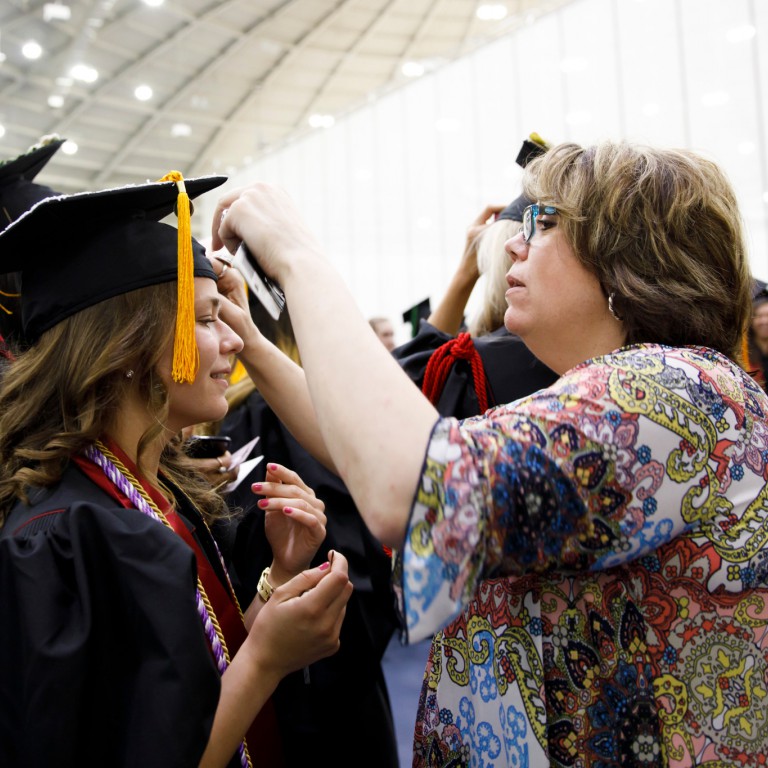 IU Southeast alumna Chris Hensley, right helps nursing graduate Shelby Frick with her mortarboard.