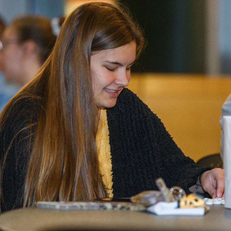 A young woman smiles while filling out her bingo card.