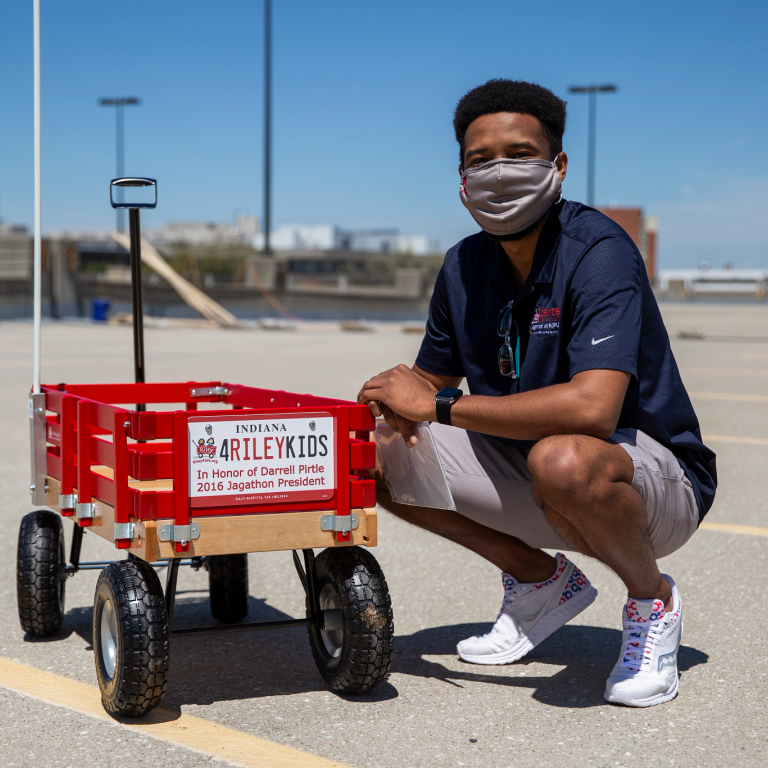 Darrell Pirtle kneels next to wagon with a sign in his honor.