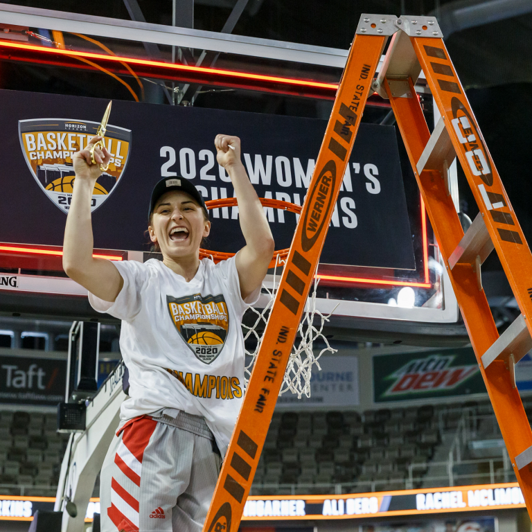 A woman stands on a ladder with a piece of net cut from a basketball goal