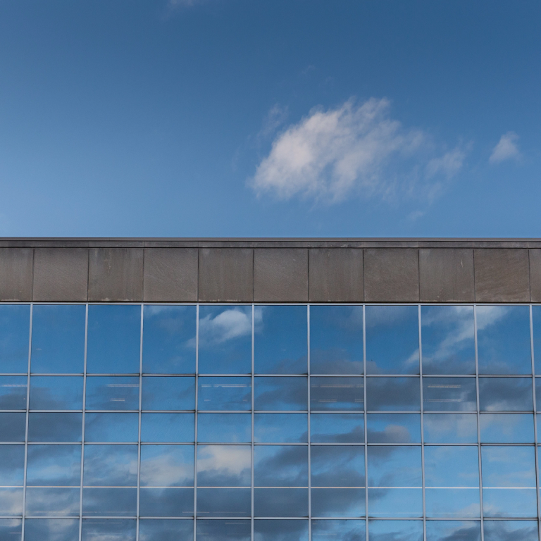 a building's windows are reflecting bright blue with the sky