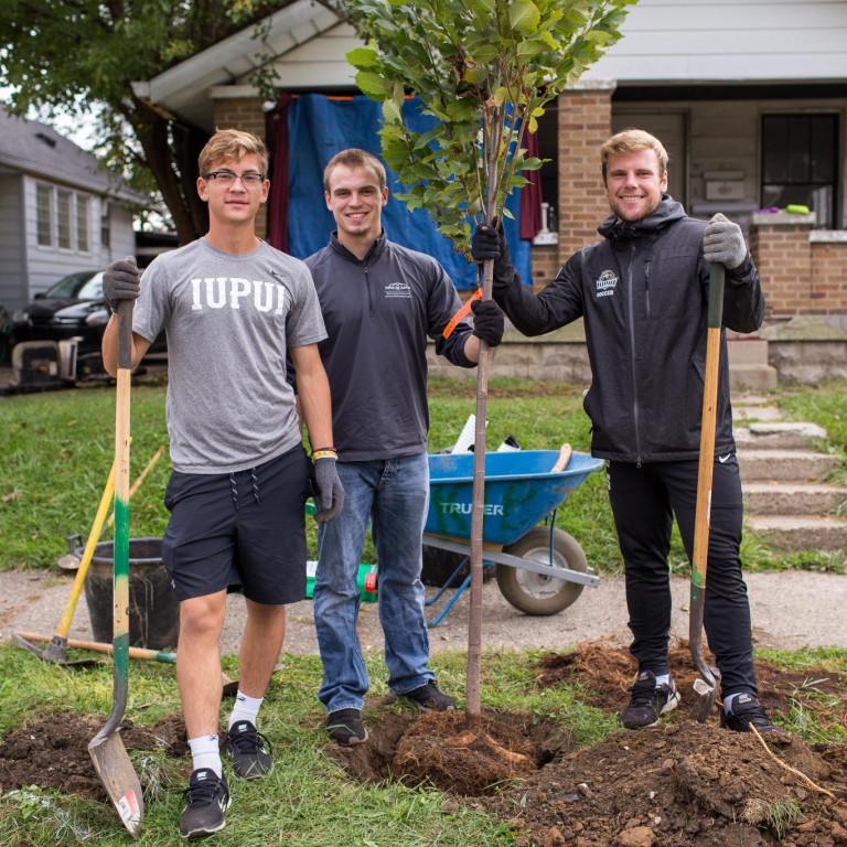 Students pose for a picture while planting a tree.