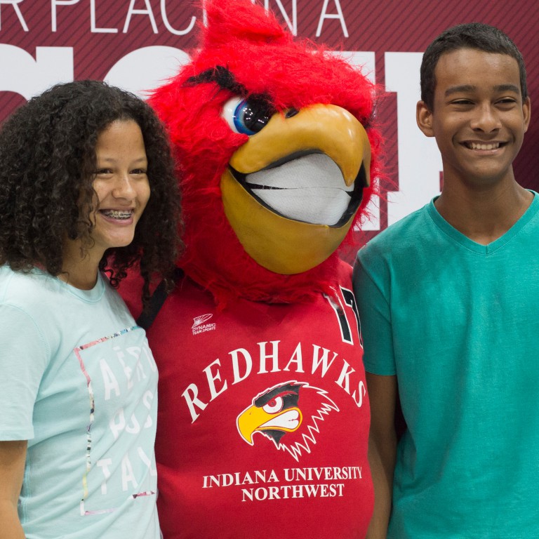 Two students stand with IU Northwest's Rufus the Redhawk mascot.
