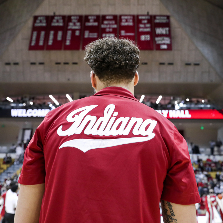 An IU basketball player on the court with red-and-white banners high in the background