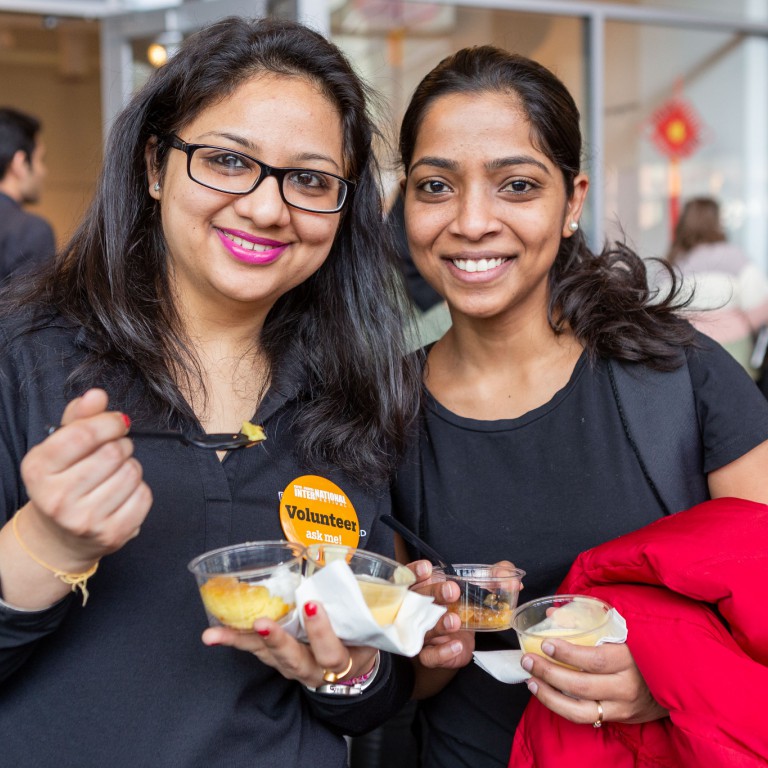 Two students pose while they eat their international food samples