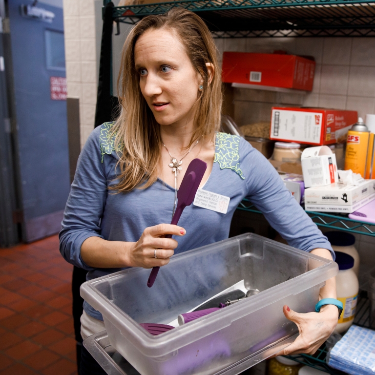 Rachel Noirot with a container of food utensils in a kitchen