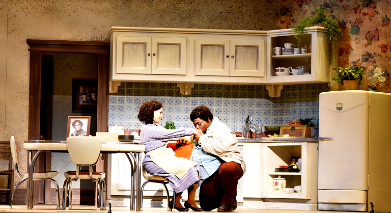 An actor kneels to kiss the hand of an actress during a performance on stage