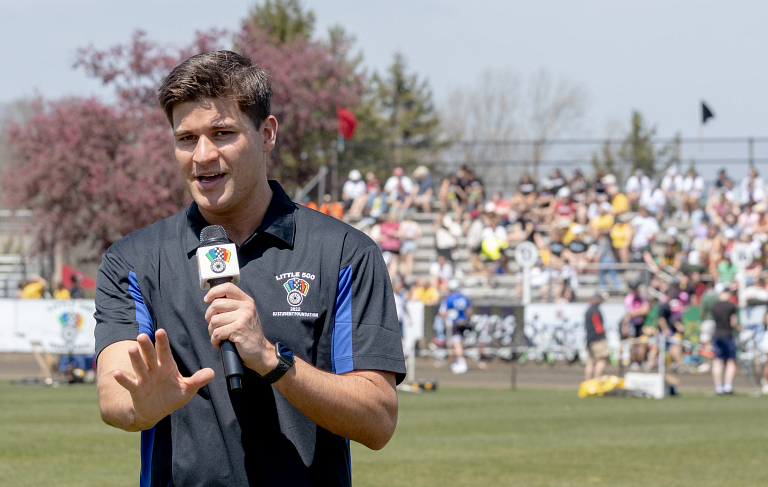 A man speaks into a microphone while standing on the infield of a cycling track.