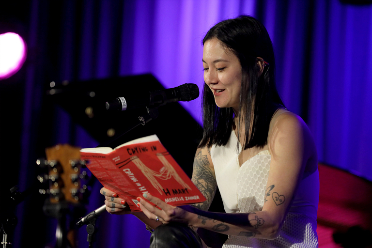 A woman reads a book aloud into a microphone. 