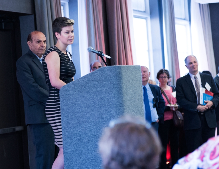 With Salman Alani standing behind her, student Madison O'Day speaks from a podium.