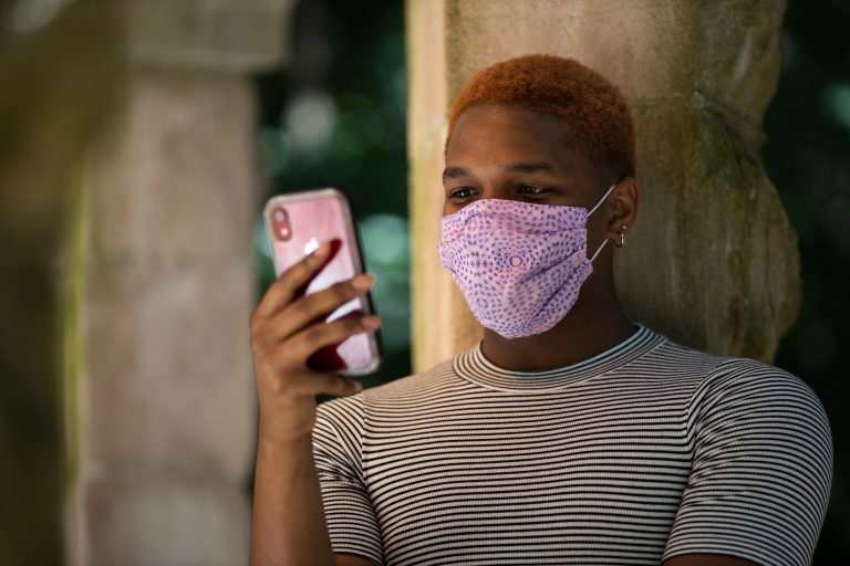 A student wearing a face mask looks at their phone