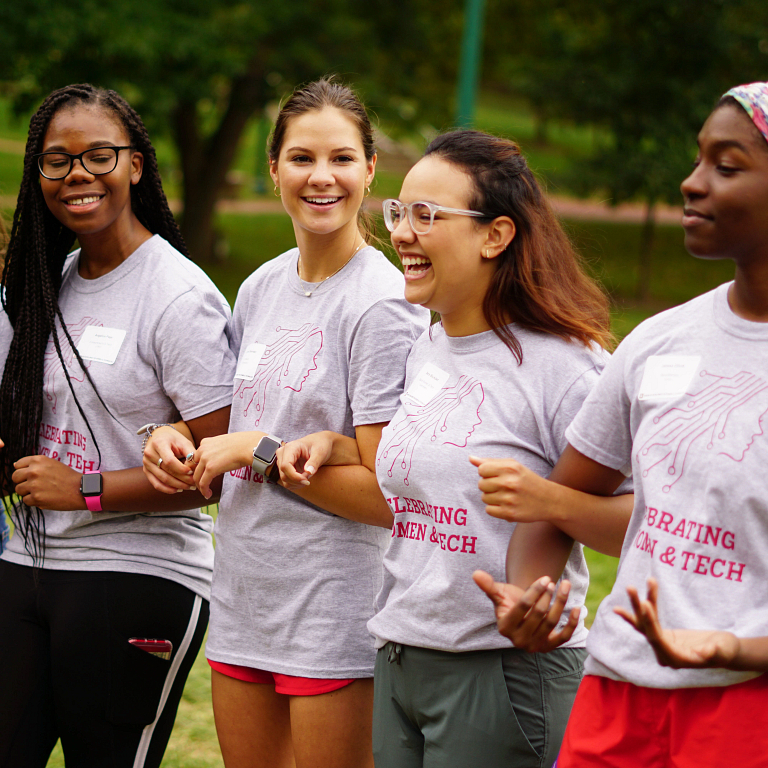 Four female students walk arm in arm