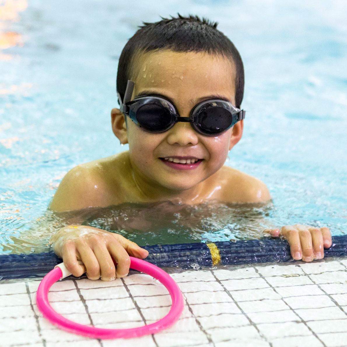 A young swimming student smiles at the edge of the pool