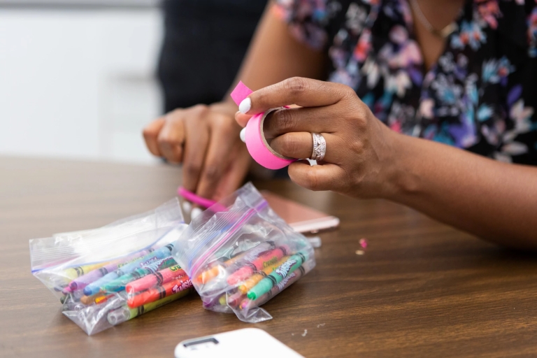 A woman uses pink tape, scissors and crayons for an art project