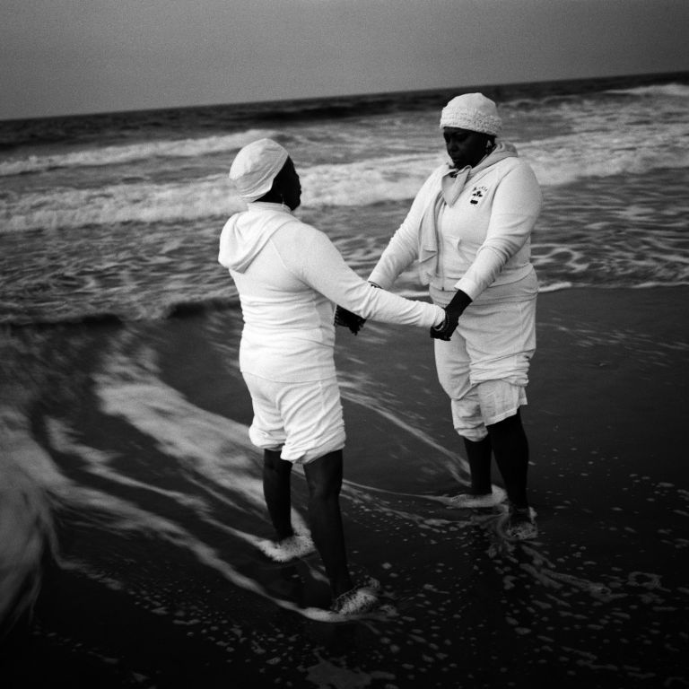 Two women hold hands on the beach.
