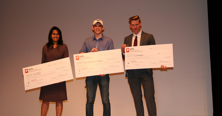 Three IUPUI students hold oversized checks