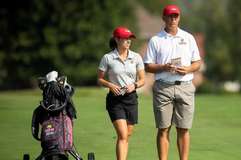 Male golf coach talks with a female golfer during a match