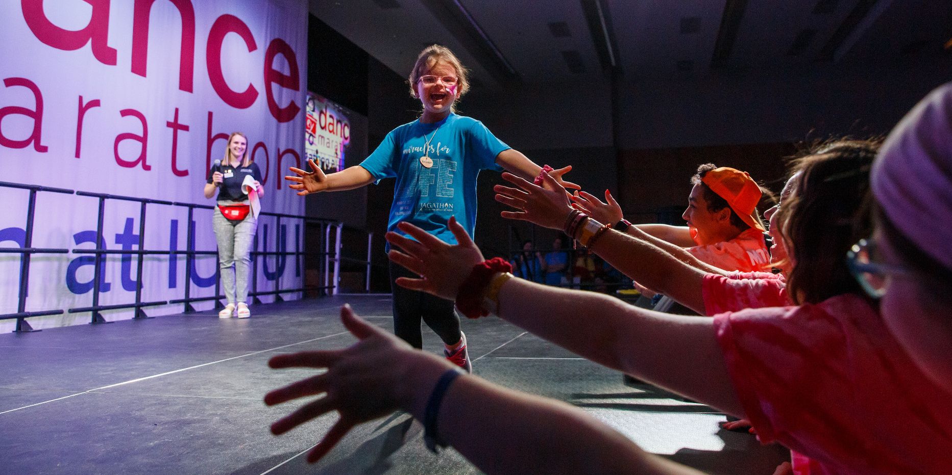 A kid runs across the stage and high-fives people in the crowd at Jagathon