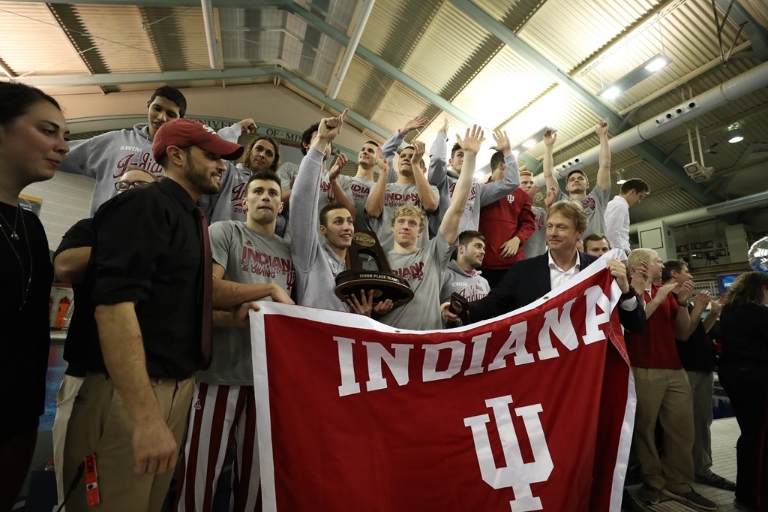 IU men's swimming and diving team gathers for a photo with an IU flag