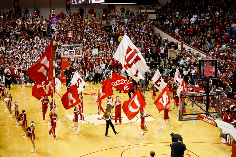 a large group of cheerleaders and red and white iu flags are across the court