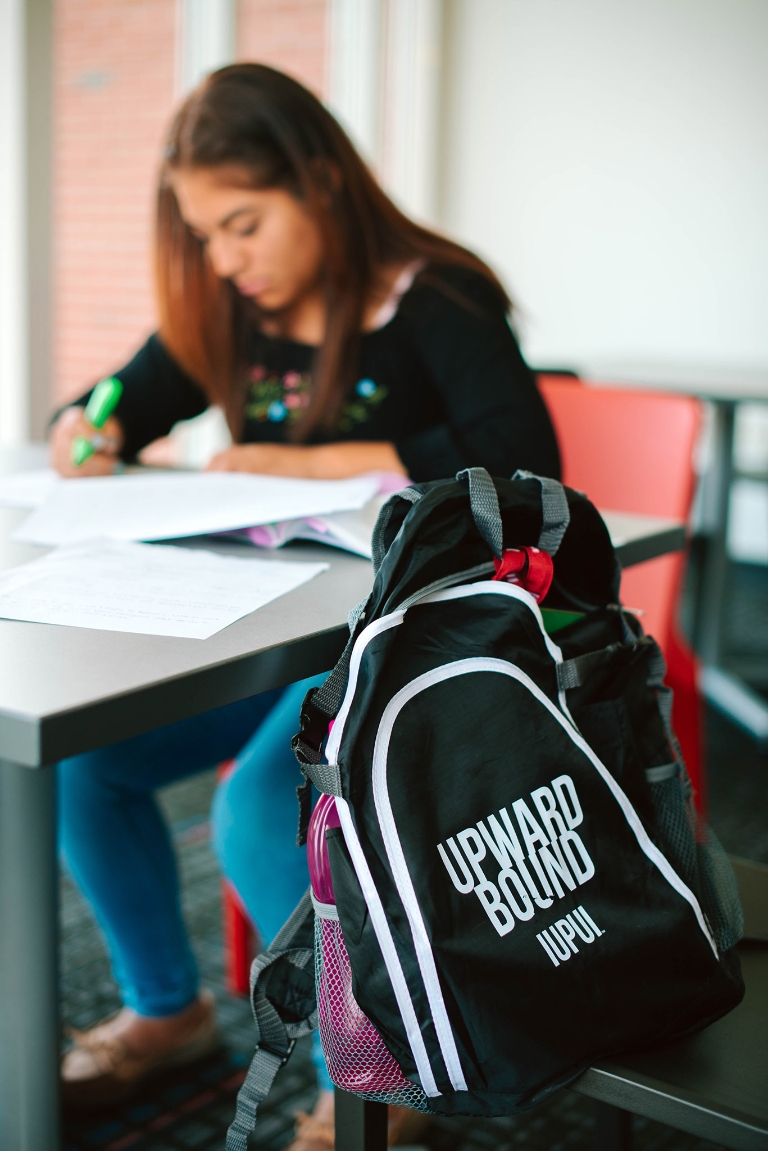 A girl studies at a table with an Upward Bound backpack in the foreground.