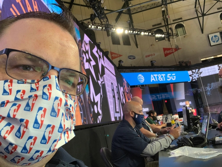 a man wearing a mask is sitting at the scorer's table at an NBA game