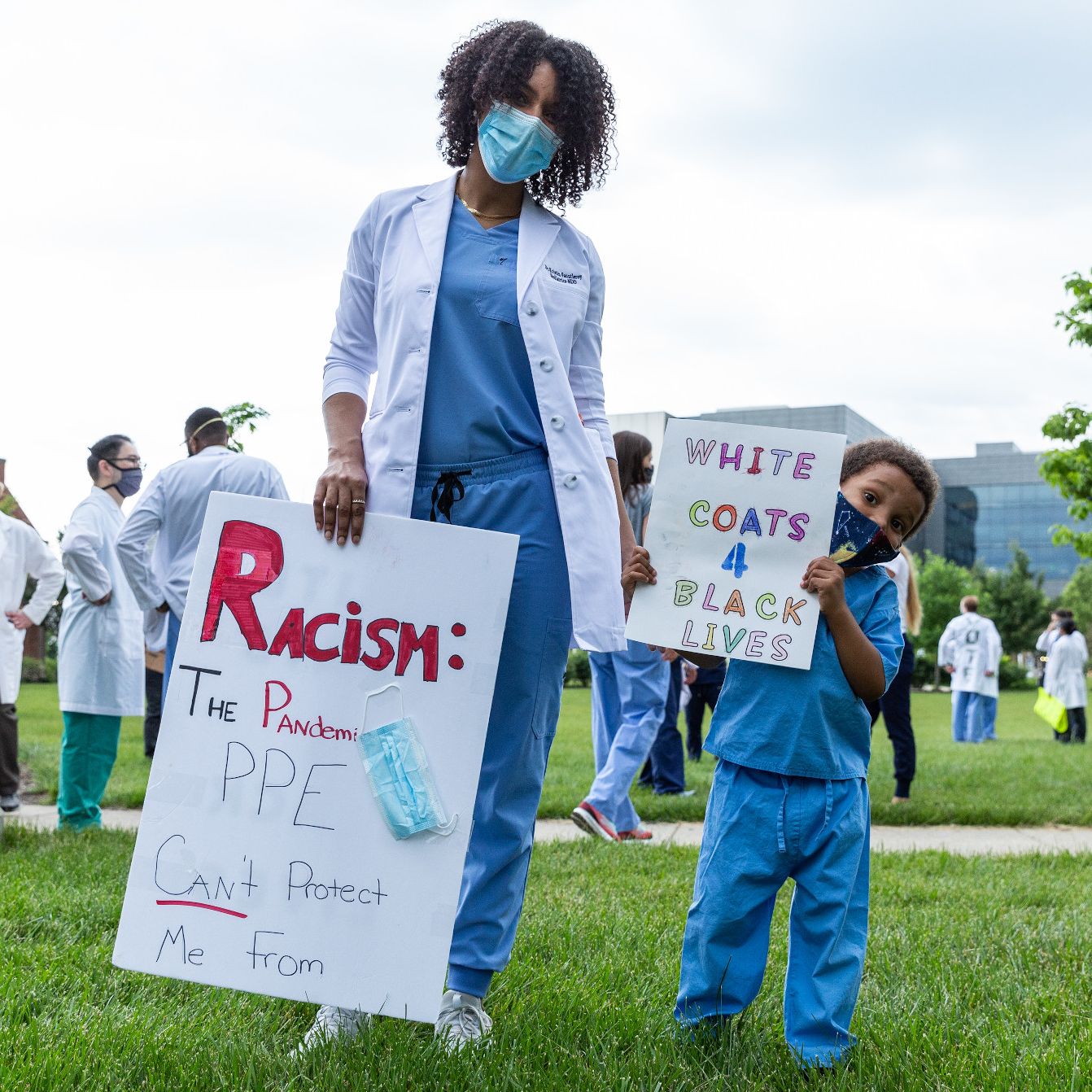 A woman and child wearing scrubs and face masks are holding signs