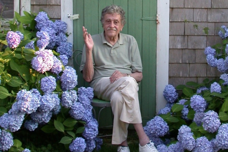 Author Kurt Vonnegut sits on a stool, framed by Hydrangea flowers