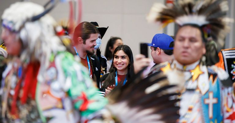 Students from the Powwow Committee stand in the middle of a group of traditional dancers.