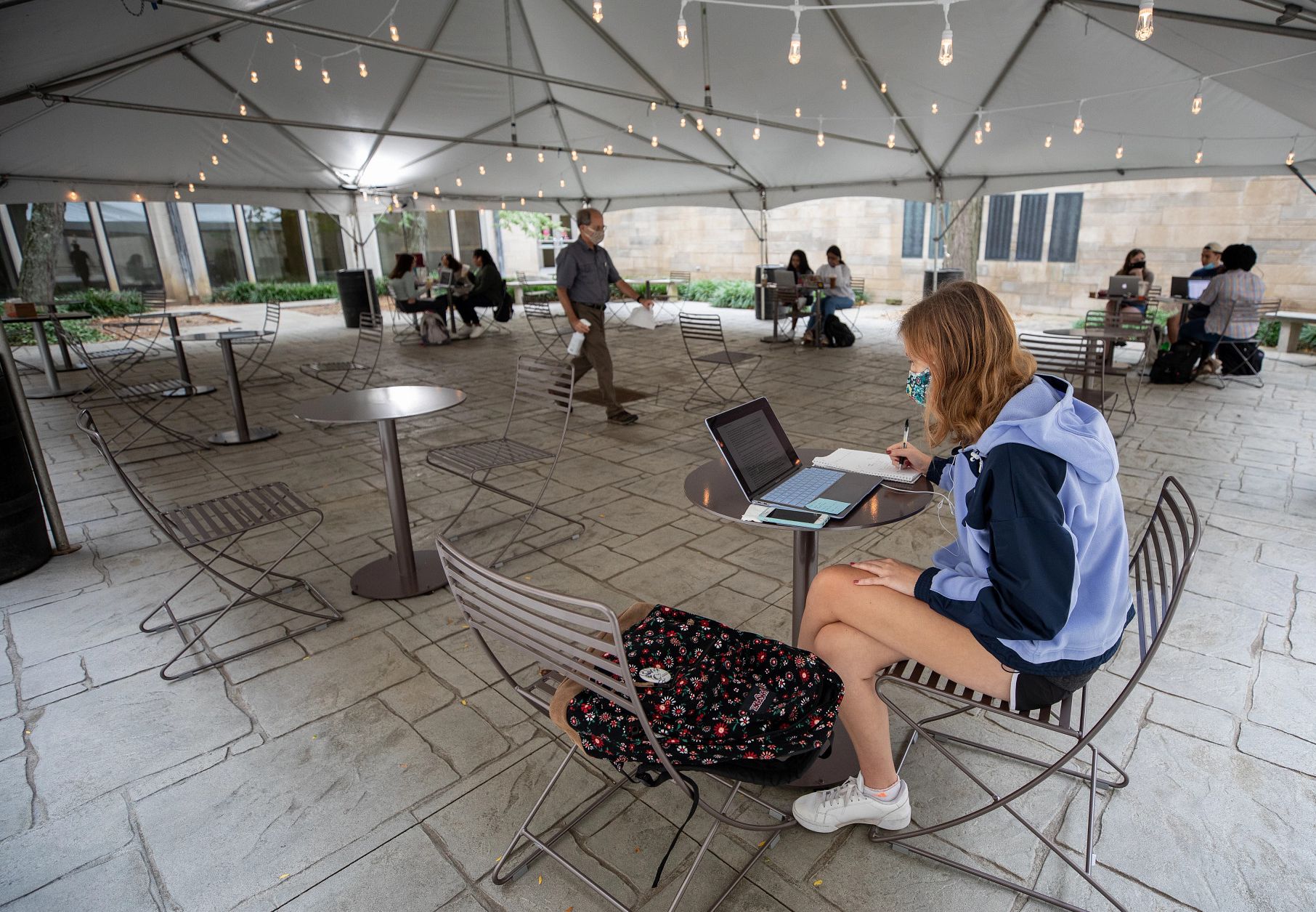 a masked female studies with a laptop under a tent