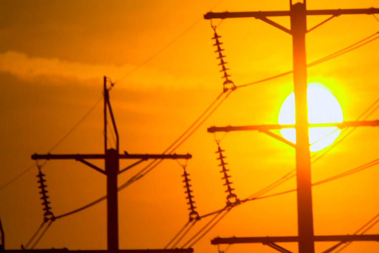 Power lines silhouetted against a bright sun and orange sky
