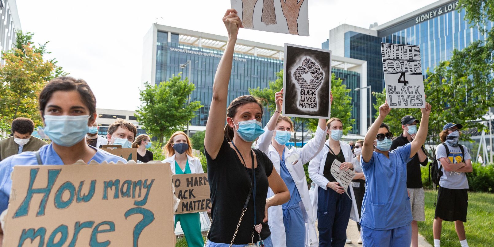 A collection of people wearing masks are standing holding signs