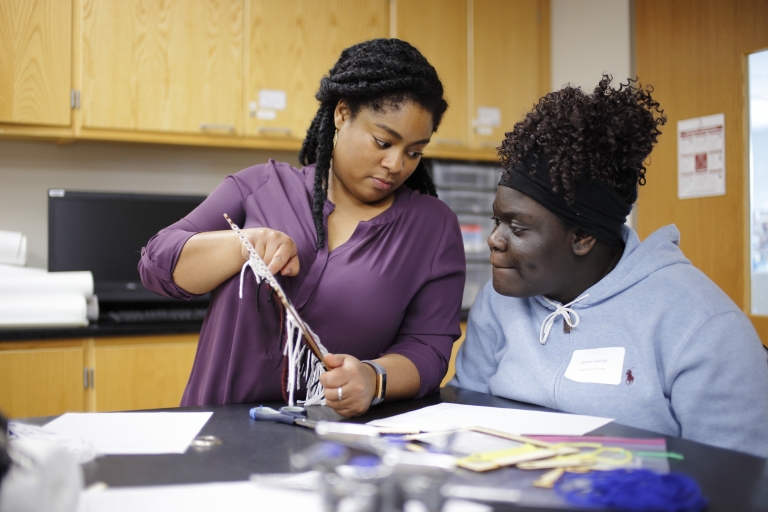 A doctoral candidate helps a high school student with a math weaving activity. 