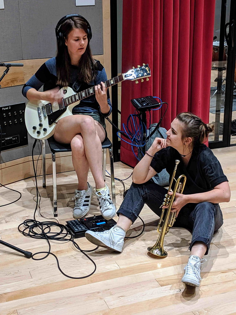 Woman plays guitar next to woman holding trumpet