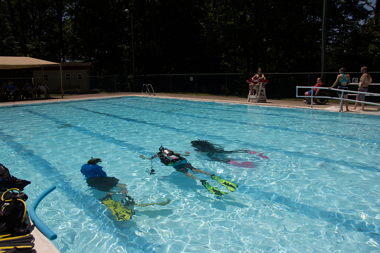 A camper and two instructors swim the length of the pool
