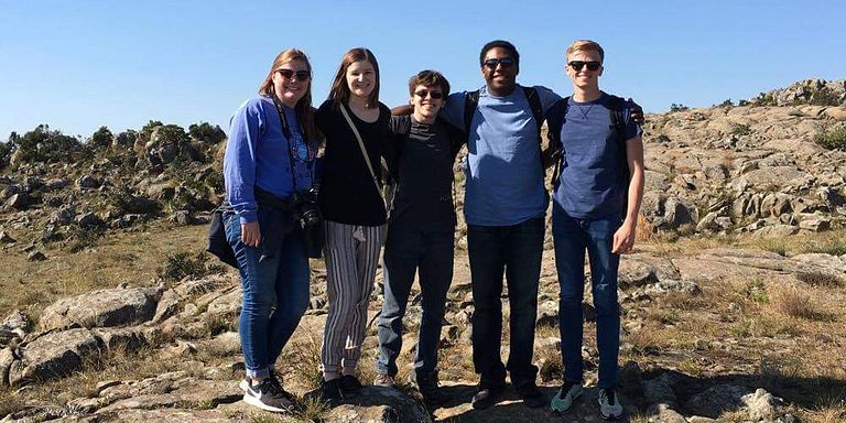 A group of five students pose in a rock outcropping in Africa.