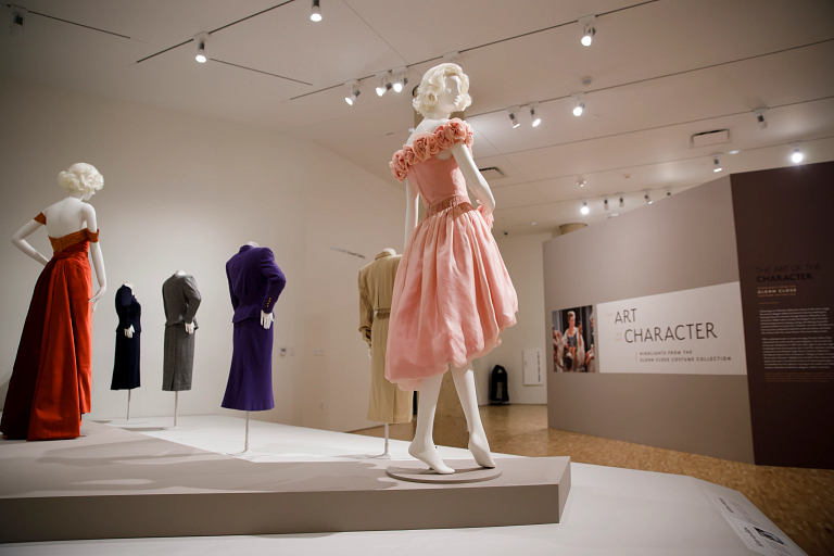 A pink silk organza dress on a mannequin in the center of an exhibition of other dresses