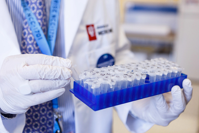 A closeup of gloved hands holding a box of test tubes with numbers on the lids