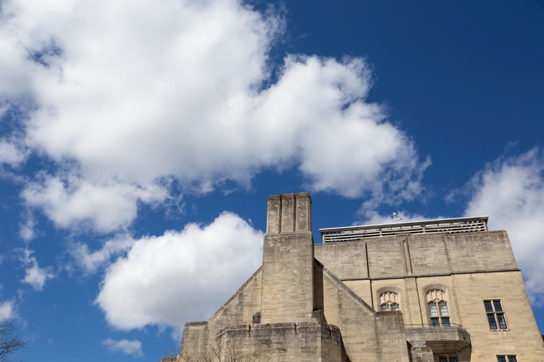 A blue sky with puffy white clouds and a limestone building in the foreground.