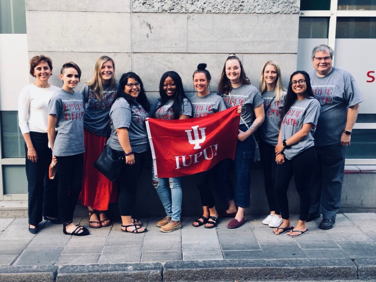 A group of students hold a red IUPUI flag on a sidewalk.