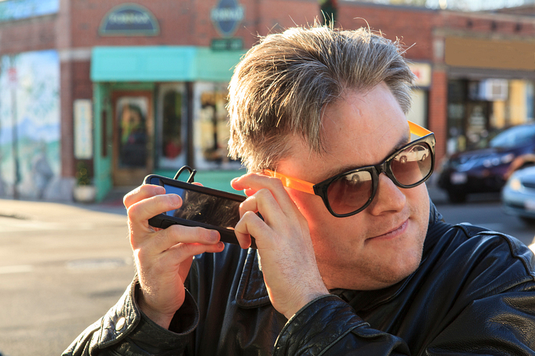 Blind person holds mobile phone up to his ear, with his fingers poised over the phone's keyboard